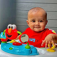 Yashvik joined the competition — help win amazing prizes! activity_center, baby, background, bright_colors, child, colorful, cute, expression, face, hand, happy, indoor, infant, mirror, person, play, red_shirt, smiling, toy, wood_paneling