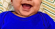 Yashvik is registered to the contest to win money with this photo: apparel, baby, blue_shirt, cheerful, child, closeup, cute, face, happy, head, indoors, infant, laying_down, patterned_background, pediatrics, person, portrait, smiling, text_on_clothing, young_child