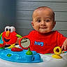 Yashvik is registered to the contest to win money with this photo: activity_center, baby, bright_colors, child, colorful, curious, expression, face, hug_text, indoor, mirror, plastic_toy, playtime, red_shirt, seat, smiling, toddler, toy, wooden_wall, young_child
