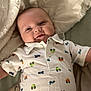 baby, infant, smiling, onesie, bed, blanket, clothing, cute, happy, child, face, lying_down, indoors, apparel, fabric, pattern, comfort, toddler, portrait, human
