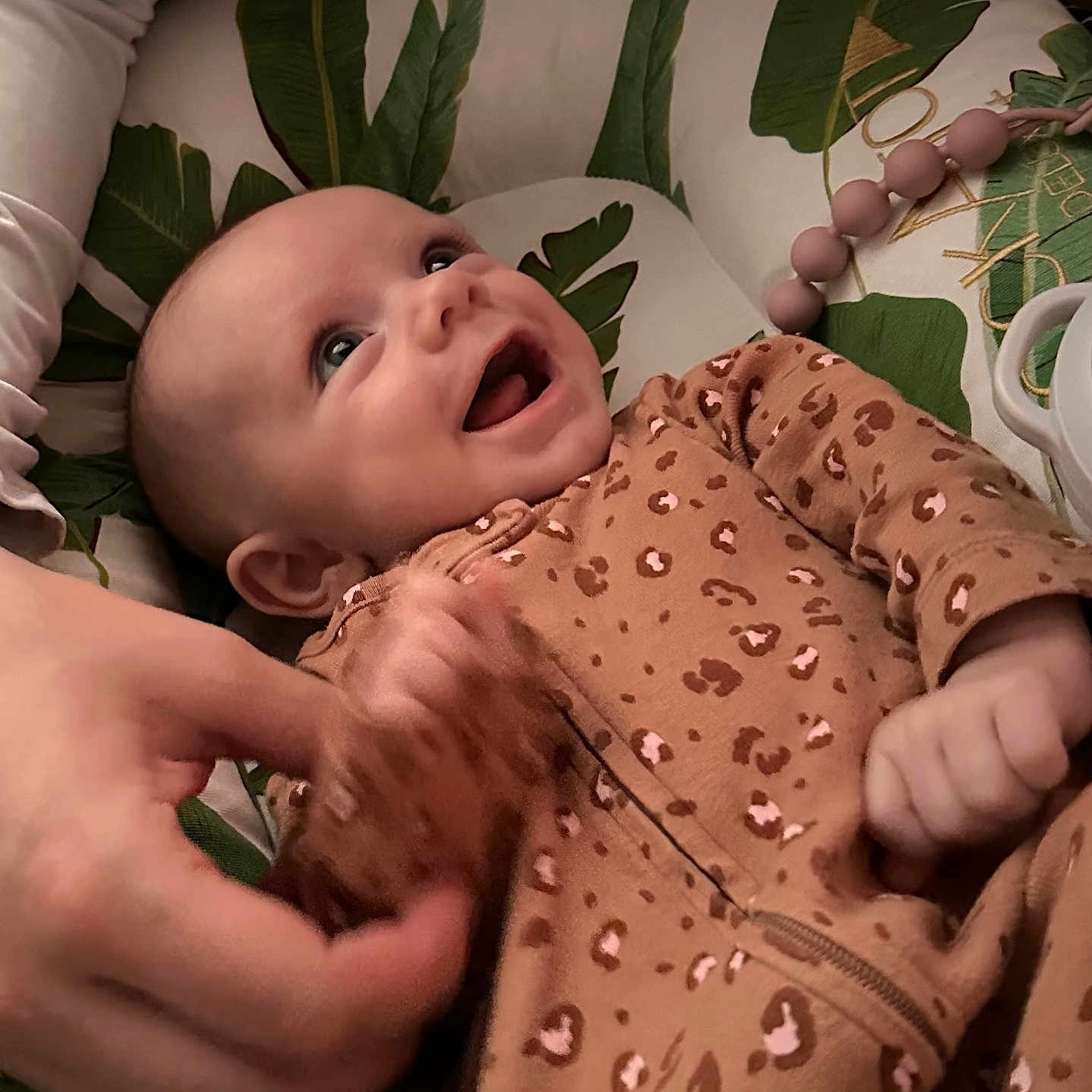 Keeleigh is registered to the contest to win money with this photo: apparel, baby, child, comfort, cushion, cute, fabric, face, hand, happy, human_hand, indoor, infant, joy, leaf_pattern, leopard_print, onesie, person, playful, smiling