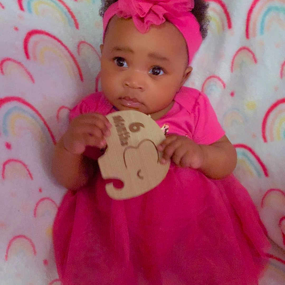 Kay'Anna is registered to the contest to win money with this photo: baby, child, clothing, colorful, curious, cute, headband, holding_object, indoors, infant, person, pink_dress, playtime, portrait, puzzle_piece, rainbow_blanket, sitting, soft_toys, toddler, young_child
