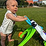 Dahïss participe au concours pour gagner de l'argent avec cette photo : background_blur, barefoot, blue_eyes, child, daylight, grass, green_toy, nature, orange_wheels, outdoor, person, playing, sleeveless_shirt, standing, summer, sunny, toddler, toy, walker, young_child