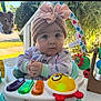 Alayah joined the competition — help win amazing prizes! baby, child, headband, bow, toy, activity_center, hands, clothing, indoor, face, blue_eyes, knitted, colorful, playtime, infant, cute, expression, person, closeup, seat
