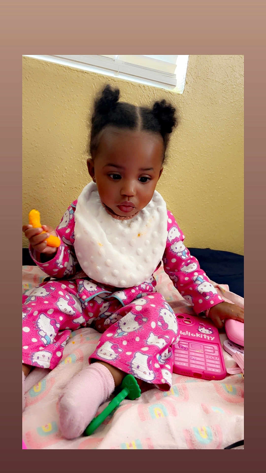 Journie is registered to the contest to win money with this photo: toddler, child, baby, pajamas, hello_kitty, bib, snack, toy_phone, pink, sock, blanket, indoor, sitting, curious, play, toy, colorful, face, hair, expression