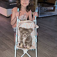 Appy a rejoint le concours — aidez-le/la à gagner de superbes lots ! child, girl, puppy, dog, stroller, indoor, floor, smiling, cute, pet, brown_hair, wood_floor, furniture, home, toy, happy, small_dog, casual_clothing, living_room, portrait