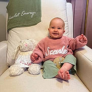 Scarlett is registered to the contest to win money with this photo: baby, smiling, child, stuffed_animal, armchair, blanket, knitwear, toy, indoor, plant, curtains, person, portrait, cute, happy, furniture, cozy, clothing, footwear, home_decor