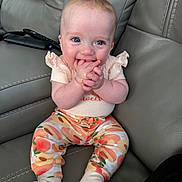 Ellie is registered to the contest to win money with this photo: baby, child, infant, smiling, sitting, couch, leather, clothing, socks, hands, face, blue_eyes, cute, happy, indoor, person, colorful_pants, patterned_clothing, skin, young
