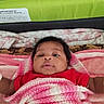 baby, infant, blanket, pink, red_clothing, bed, headboard, knit, face, expression, lying_down, indoors, soft_texture, curly_hair, skin, portrait, child, warm, cozy, sleeping_area