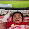baby, infant, blanket, mitten, red_shirt, smiling, face, lying_down, indoors, cushion, knit, soft_texture, happy, person, child, closeup, portrait, cozy, home, warning_label