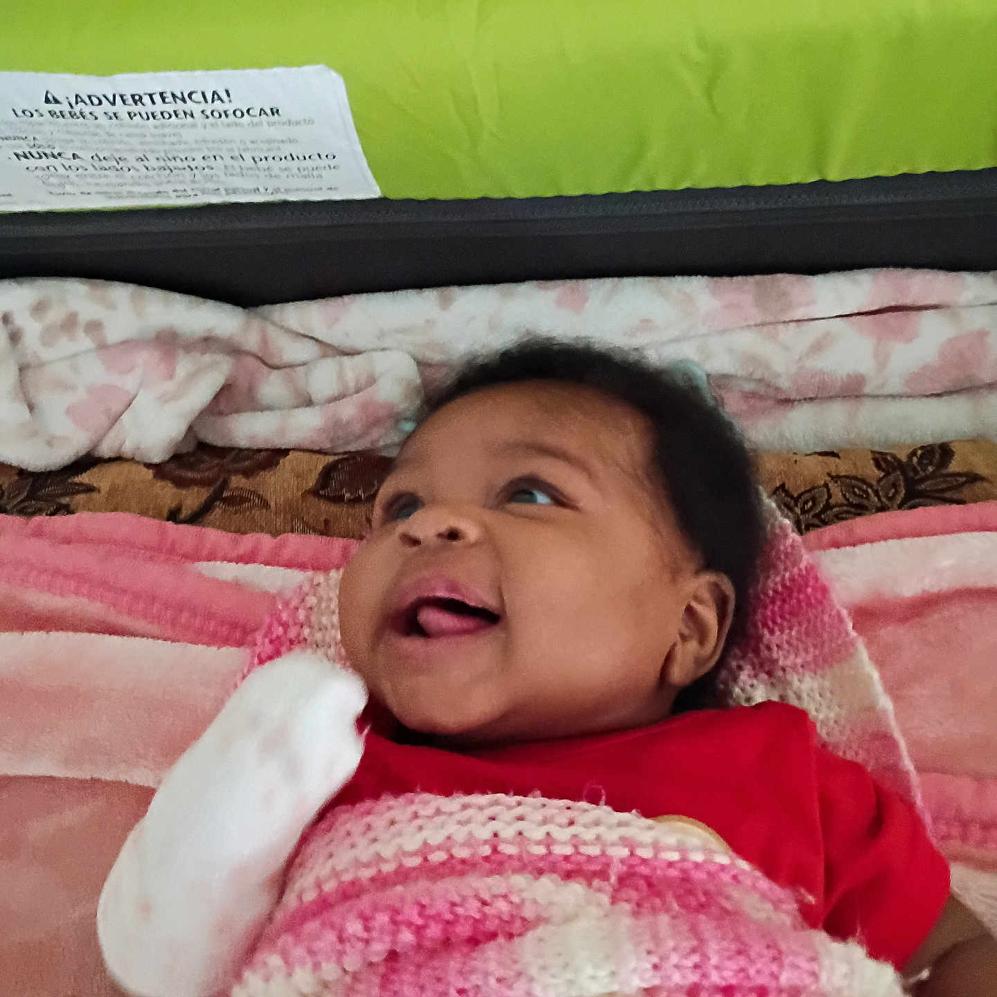 Jamie Lynn is registered to the contest to win money with this photo: baby, infant, smiling, blanket, knitted, mitten, red_clothing, lying_down, cozy, indoor, cushion, face, cute, child, portrait, happy, skin, person, head, expression