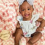 baby, child, infant, smiling, white_bow, butterfly, headband, white_outfit, pink_blanket, textured_blanket, wooden_sign, seven_months, happy, cute, sitting, tongue_out, indoors, portrait, soft_texture, young_child