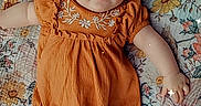 Ava joined the competition — help win amazing prizes! baby, infant, child, portrait, lying_down, smiling, orange_outfit, romper, hat, topknot, socks, floral_blanket, bed, indoor, close_up, face, eyes, arms, fashion, cute