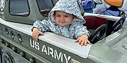 Gabrielle a rejoint le concours — aidez-le/la à gagner de superbes lots ! toddler, child, hooded_jacket, amusement_park, mini_tank, us_army, ride, smile, outdoor, playful, carnival, colorful, toy_vehicle, fun, face, person, clothing, cloudy_sky, hand, park