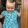 toddler, child, smiling, dress, blue, patterned_clothing, door_frame, wood, indoors, kitchen, tile_floor, person, hair_clip, happy, cute, young_child, standing, natural_light, casual, portrait