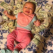 Samantha joined the competition — help win amazing prizes! baby, infant, smiling, money, dollar_bills, pink_clothing, bib, blue_socks, floral_bedspread, happy, lying_down, indoors, person, currency, cute, small_child, face, hand, footwear, background