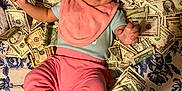 Samantha joined the competition — help win amazing prizes! baby, background, bib, blue_socks, currency, cute, dollar_bills, face, floral_bedspread, footwear, hand, happy, indoors, infant, lying_down, money, person, pink_clothing, small_child, smiling