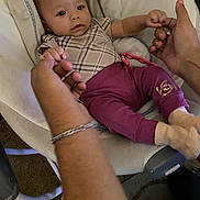 Samantha is registered to the contest to win money with this photo: adult_hands, baby, baby_seat, blanket, carpet, child, clothing, comfort, cushion, cute, footwear, hands, holding_hands, indoor, infant, person, purple_pants, relaxation, socks, toy