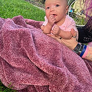 Samantha joined the competition — help win amazing prizes! baby, blanket, pink, hand, person, outdoor, grass, fence, bicycle_wheel, wristbands, curious, plush, soft_texture, holding, child, young, portrait, cute, infant, casual