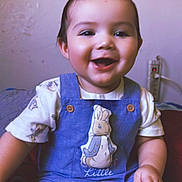 Remy is registered to the contest to win money with this photo: baby, child, smiling, happy, sitting, overalls, blue_clothing, indoor, cute, portrait, face, short_hair, bunny, illustration, tshirt, young_child, skin, person, infant, mohaawk
