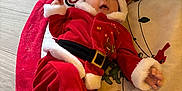 Ellie joined the competition — help win amazing prizes! baby, infant, christmas, santa_outfit, red_clothing, white_fur_trim, holiday, gift_wrap, floor, mat, festive, cute, child, person, indoor, seasonal, celebration, holiday_decor, smiling, lying_down