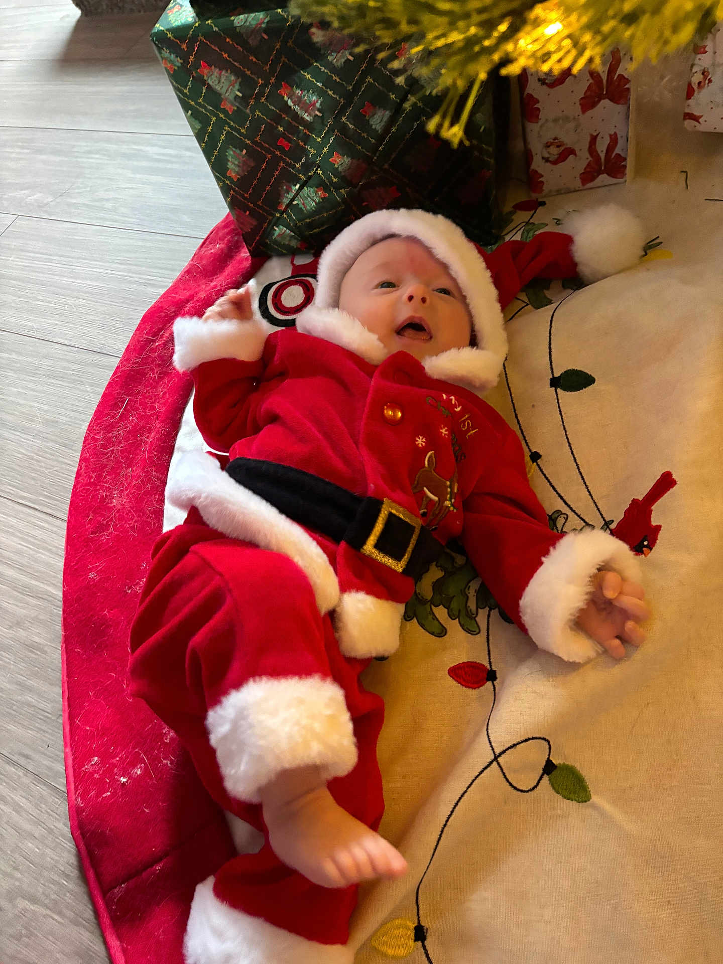 Ellie joined the competition — help win amazing prizes! baby, infant, christmas, santa_outfit, red_clothing, white_fur_trim, holiday, gift_wrap, floor, mat, festive, cute, child, person, indoor, seasonal, celebration, holiday_decor, smiling, lying_down