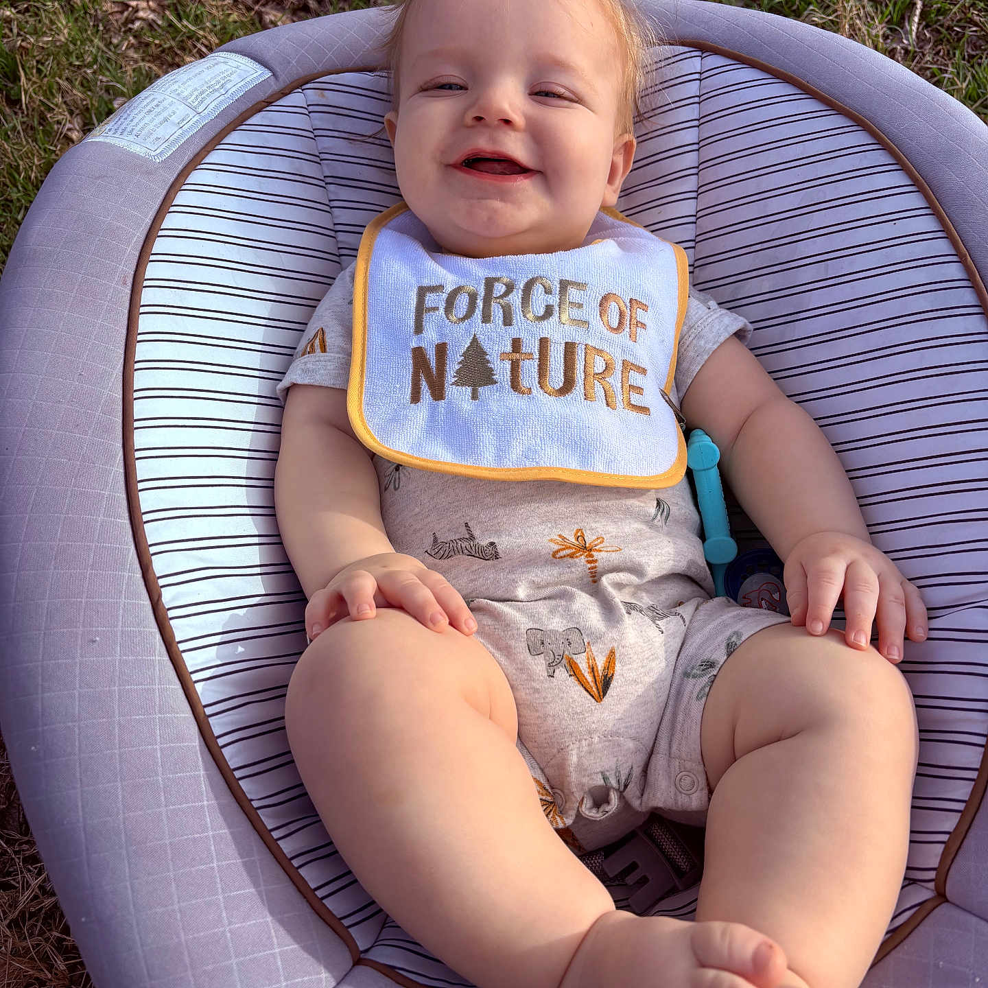 Ryker joined the competition — help win amazing prizes! baby, baby_seat, bib, chubby_legs, eyes, face, grass, hand, infant, legs, onesie, outdoor, pacifier, patterned_clothing, seat_padding, skin, smile, smiling, toes, toy