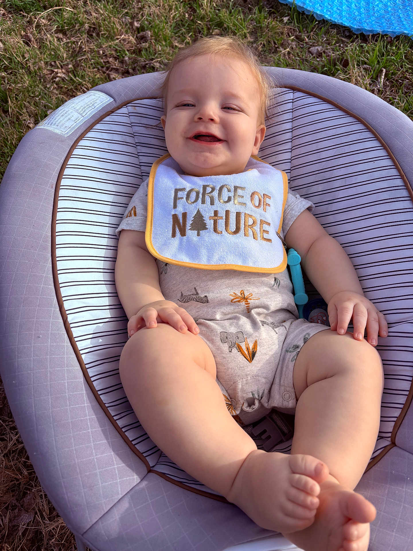 Ryker joined the competition — help win amazing prizes! baby, infant, smiling, bib, baby_seat, grass, outdoor, legs, toes, chubby_legs, onesie, patterned_clothing, pacifier, hand, face, eyes, smile, skin, toy, seat_padding