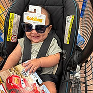 Izan is registered to the contest to win money with this photo: baby, car_seat, shopping_cart, sunglasses, toy, packaging, smile, child, infant, seatbelt, store, retail, plastic, hand, clothing, person, happy, indoor, product, cart
