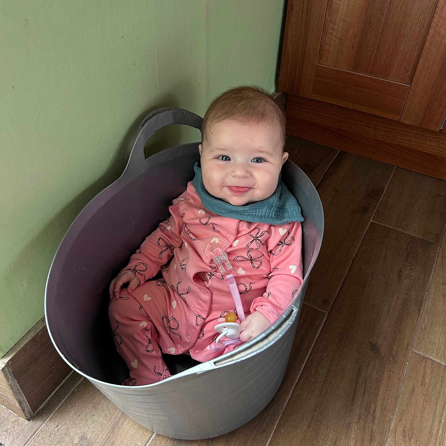 Megan joined the competition — help win amazing prizes! baby, bucket, cabinet, child, cute, face, floor, green_wall, happy, home, indoor, infant, pacifier, pajamas, person, pink_clothing, sitting, smile, toy, wood_floor