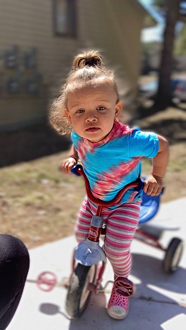 Mia is registered to the contest to win money with this photo: automotive_tire, baby_toddler_clothing, bicycle_accessory, child, cycling, dress, electric_blue, eyewear, face, fun, grass, happy, leisure, person, recreation, smile, street_fashion, t_shirt, tire, toddler