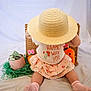 Emory is registered to the contest to win money with this photo: back_view, basket, carrot_toy, child, cute, dollar_bills, green_shredded_paper, hat, indoor, mug, pink_socks, playful, plush_toys, shirt, sitting, skirt, straw_hat, text_on_shirt, toddler, white_background
