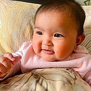 Eliana is registered to the contest to win money with this photo: baby, blanket, cheeks, child, cozy, cute, expression, face, head, human, indoors, infant, looking_away, pillow, pink_sweater, portrait, smiling, soft_texture, warm_colors, young