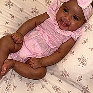 Riahleigh is registered to the contest to win money with this photo: baby, infant, smiling, pink_outfit, headband, lying_down, floral_pattern, bedspread, cute, child, happy, skin, face, hands, feet, indoors, portrait, toddler, young_child, sleepwear