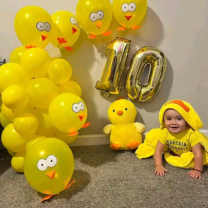 Elian is registered to the contest to win money with this photo: architecture, baby, balloon, building, clothing, face, hat, head, number, outdoors, people, person, photography, portrait, shelter, sitting, symbol, text