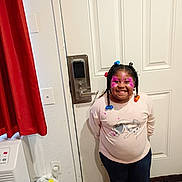Dariyanna Bernal is registered to the contest to win money with this photo: child, smiling, face_paint, braided_hair, beads, indoor, door, shirt, jeans, happy, standing, wall, curtain, plastic_bags, floor, light_switch, lock, handle, person, portrait