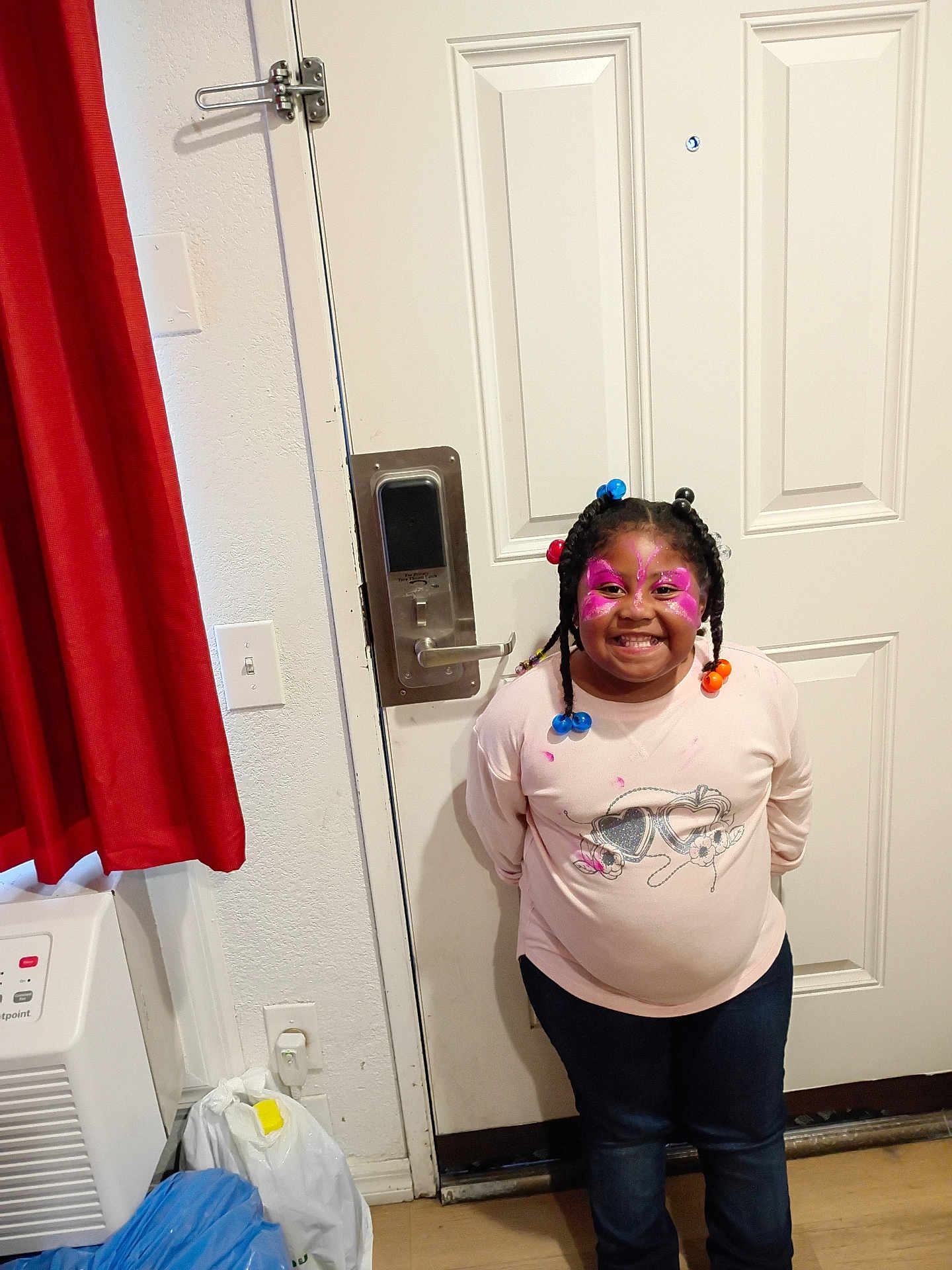 Dariyanna Bernal is registered to the contest to win money with this photo: child, smiling, face_paint, braided_hair, beads, indoor, door, shirt, jeans, happy, standing, wall, curtain, plastic_bags, floor, light_switch, lock, handle, person, portrait