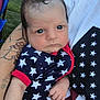 baby, infant, person, clothing, stars, tattoo, arm, hand, blue, red, white, outdoor, grass, car, portrait, closeup, face, expression, holding, sitting