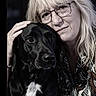 affection, animal, black_dog, calm, close_up, companionship, dog, face, glasses, hand, human, indoor, intimacy, long_hair, love, patterned_shirt, pet, portrait, white_chest_patch, woman