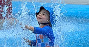 Javier joined the competition — help win amazing prizes! toddler, child, water, splash, swimsuit, blue, hat, playground, outdoor, fun, smile, happy, summer, sitting, water_splash, recreation, park, youth, person, cute