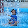 toddler, child, water, splash, swimsuit, blue, hat, playground, outdoor, fun, smile, happy, summer, sitting, water_splash, recreation, park, youth, person, cute