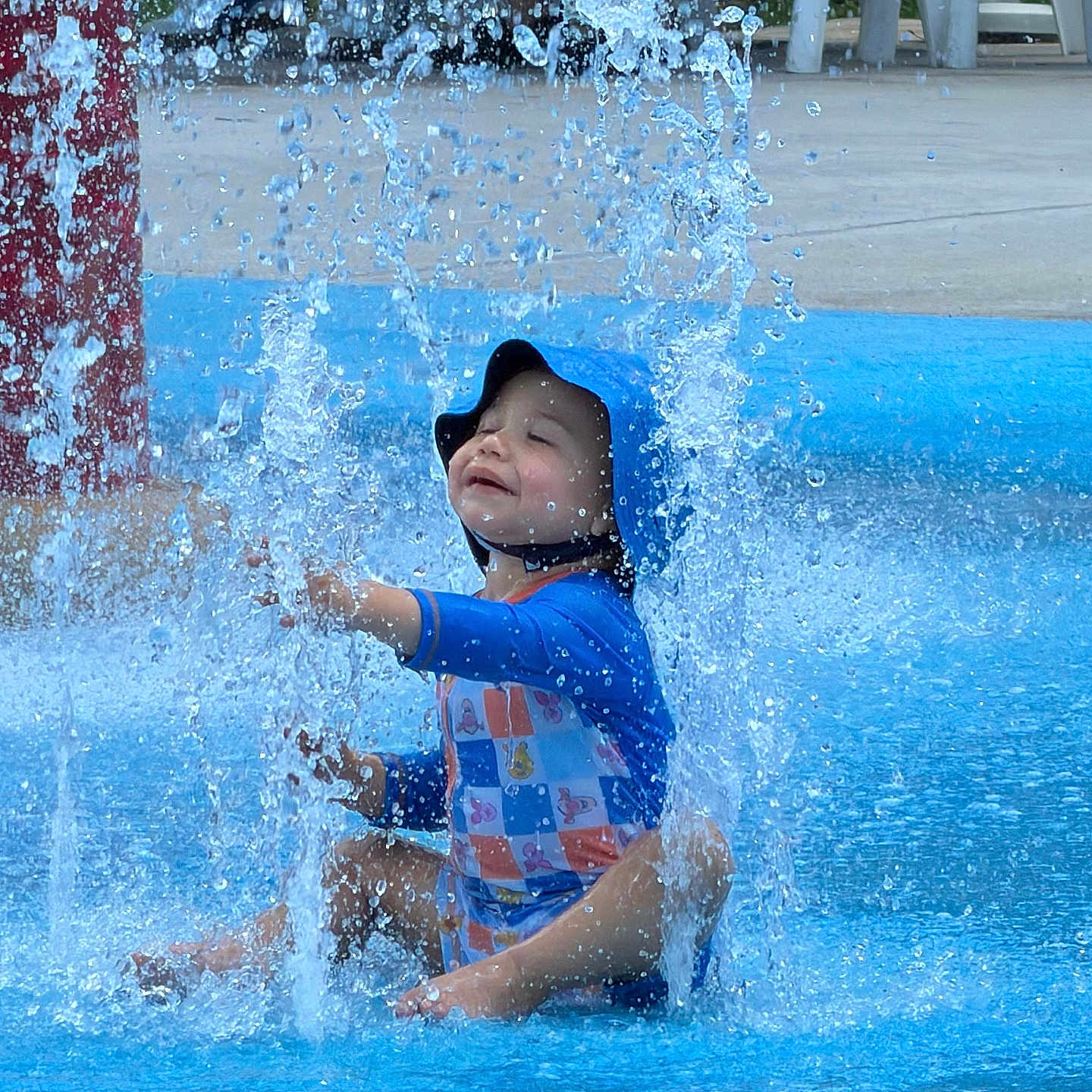 Javier joined the competition — help win amazing prizes! toddler, child, water, splash, swimsuit, blue, hat, playground, outdoor, fun, smile, happy, summer, sitting, water_splash, recreation, park, youth, person, cute