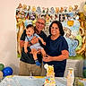child, toddler, adult, grandparents, birthday_cake, cupcakes, party, celebration, balloons, table, glasses, smile, happy, decorations, banner, indoor, family, holding, food, winnie_the_pooh