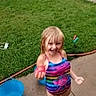 child, girl, swimsuit, colorful_clothing, water_play, outdoor, grass, bucket, sidewalk, wet_surface, summer, fun, smiling, blond_hair, playful, water_toy, happy, young, person, daylight