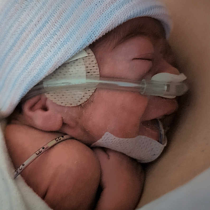 Zander is registered to the contest to win money with this photo: baby, blanket, care, closeup, cute, hat, health, hospital, hospital_gown, infant, love, medical, nasal_cannula, newborn, oxygen_tube, parent, person, skin, sleeping, tenderness