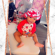 Eleigha joined the competition — help win amazing prizes! baby, child, hat, strawberry_pattern, table, smile, indoor, clothing, person, sitting, happy, footwearless, pink, red, background, plastic_bag, floor, chair, portrait, cute