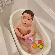 Lise participe au concours pour gagner de l'argent avec cette photo : baby, bathtub, bathroom, water, toy, child, cup, bath, toddler, plastic, orange, yellow, green, pink, cute, indoor, skin, wet_hair, looking_up, small_bathtub