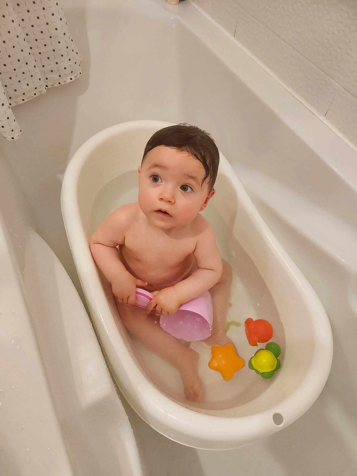 Lise participe au concours pour gagner de l'argent avec cette photo : baby, bathtub, bathroom, water, toy, child, cup, bath, toddler, plastic, orange, yellow, green, pink, cute, indoor, skin, wet_hair, looking_up, small_bathtub