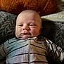 baby, child, face, onesie, striped_clothing, blanket, pillow, indoor, portrait, infant, cute, chubby_cheeks, cozy, soft_texture, young_child, relaxed, smiling, person, head, furniture