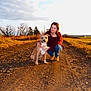 Nugget joined the competition — help win amazing prizes! woman, dog, dirt_road, outdoor, sunset, grass, trees, nature, casual_clothing, glasses, crouching, pet, field, sky, clouds, sunlight, golden_hour, landscape, animal, companion